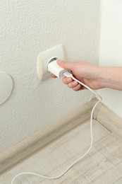 Photo of Woman plugging USB power adapter with charge cable into electrical socket indoors, closeup