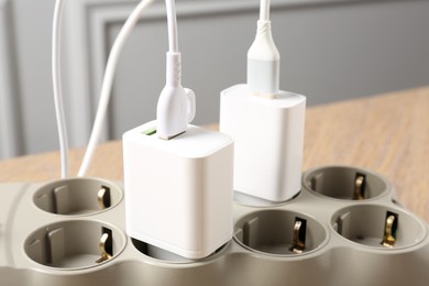 Photo of USB adapters with charge cables in power strip on wooden table indoors, closeup