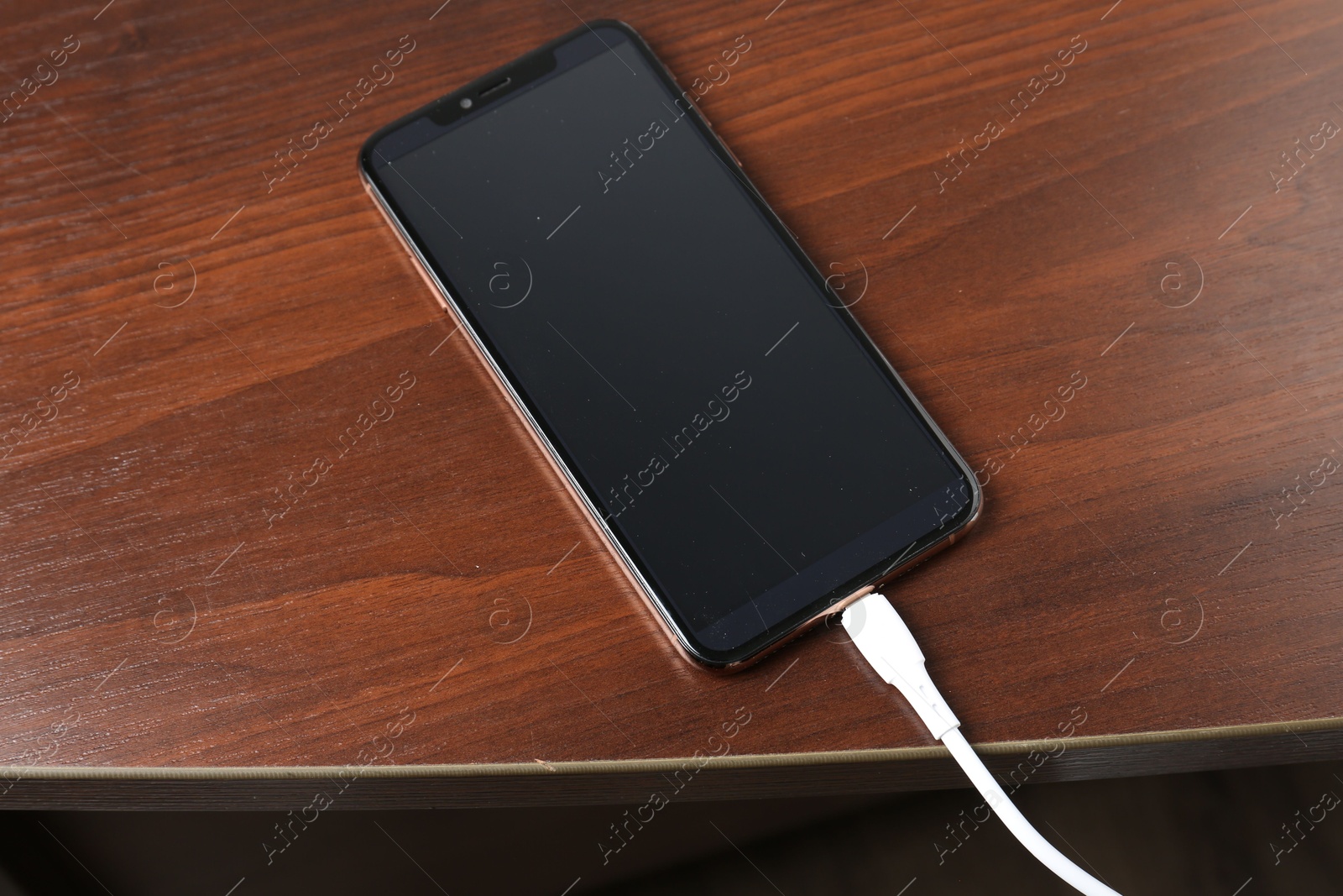 Photo of Smartphone charging from cable on wooden table, above view