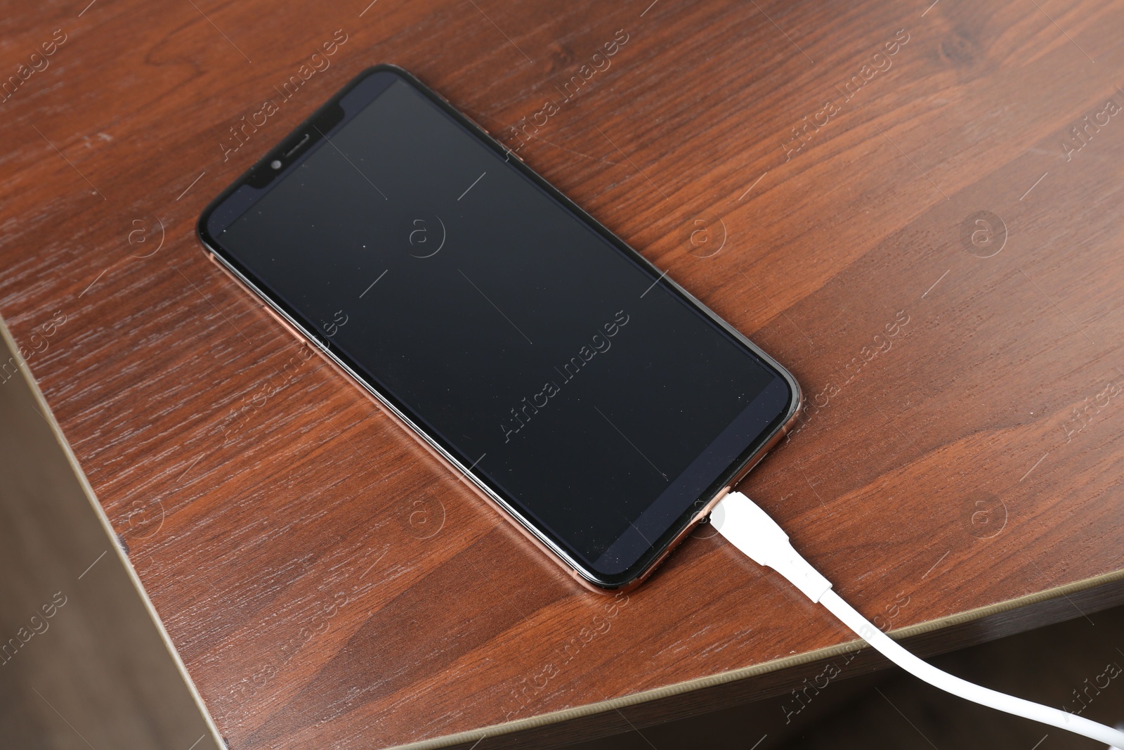 Photo of Smartphone charging from cable on wooden table, above view