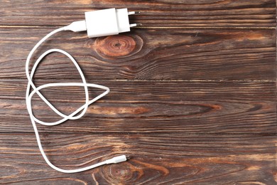 Photo of USB power adapter with charge cable on wooden table, top view. Space for text