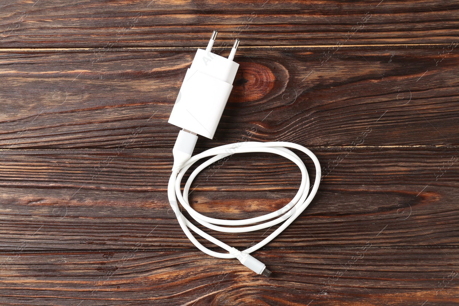 Photo of USB power adapter with charge cable on wooden table, top view