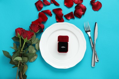 Photo of Beautiful setting for romantic dinner, engagement ring and roses on light blue background, flat lay