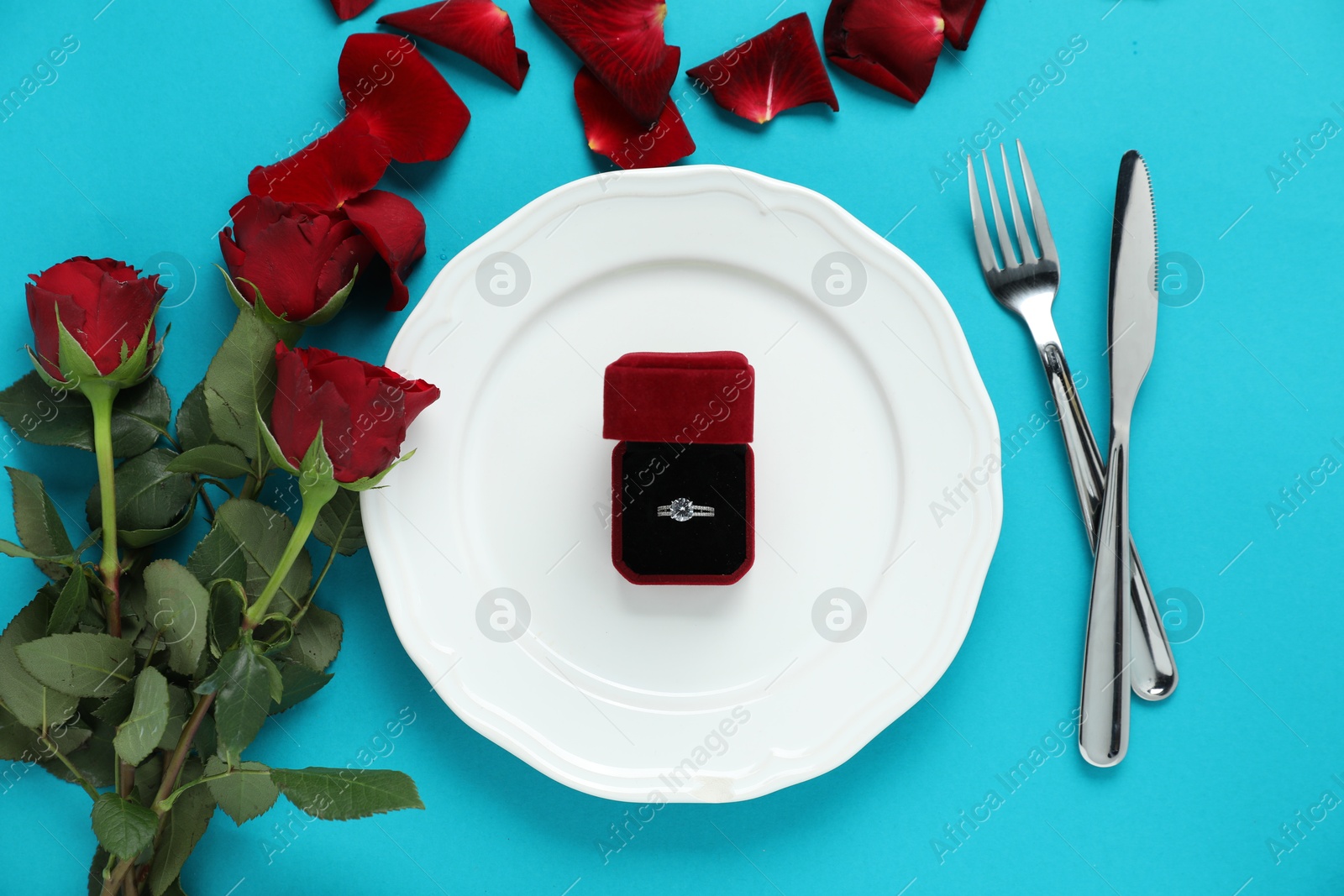 Photo of Beautiful setting for romantic dinner, engagement ring and roses on light blue background, flat lay