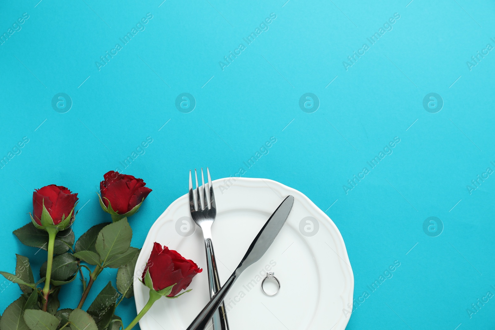 Photo of Beautiful setting for romantic dinner, engagement ring and roses on light blue background, flat lay. Space for text