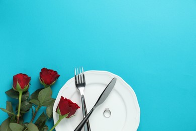 Photo of Beautiful setting for romantic dinner, engagement ring and roses on light blue background, flat lay. Space for text