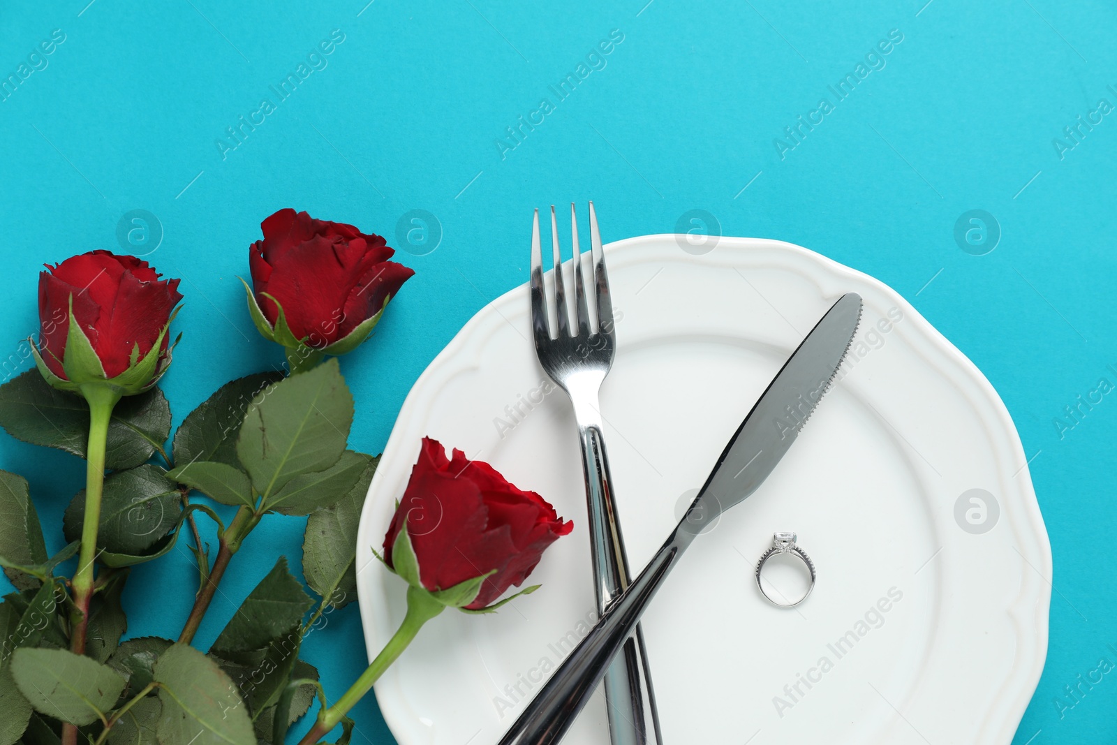 Photo of Beautiful setting for romantic dinner, engagement ring and roses on light blue background, flat lay