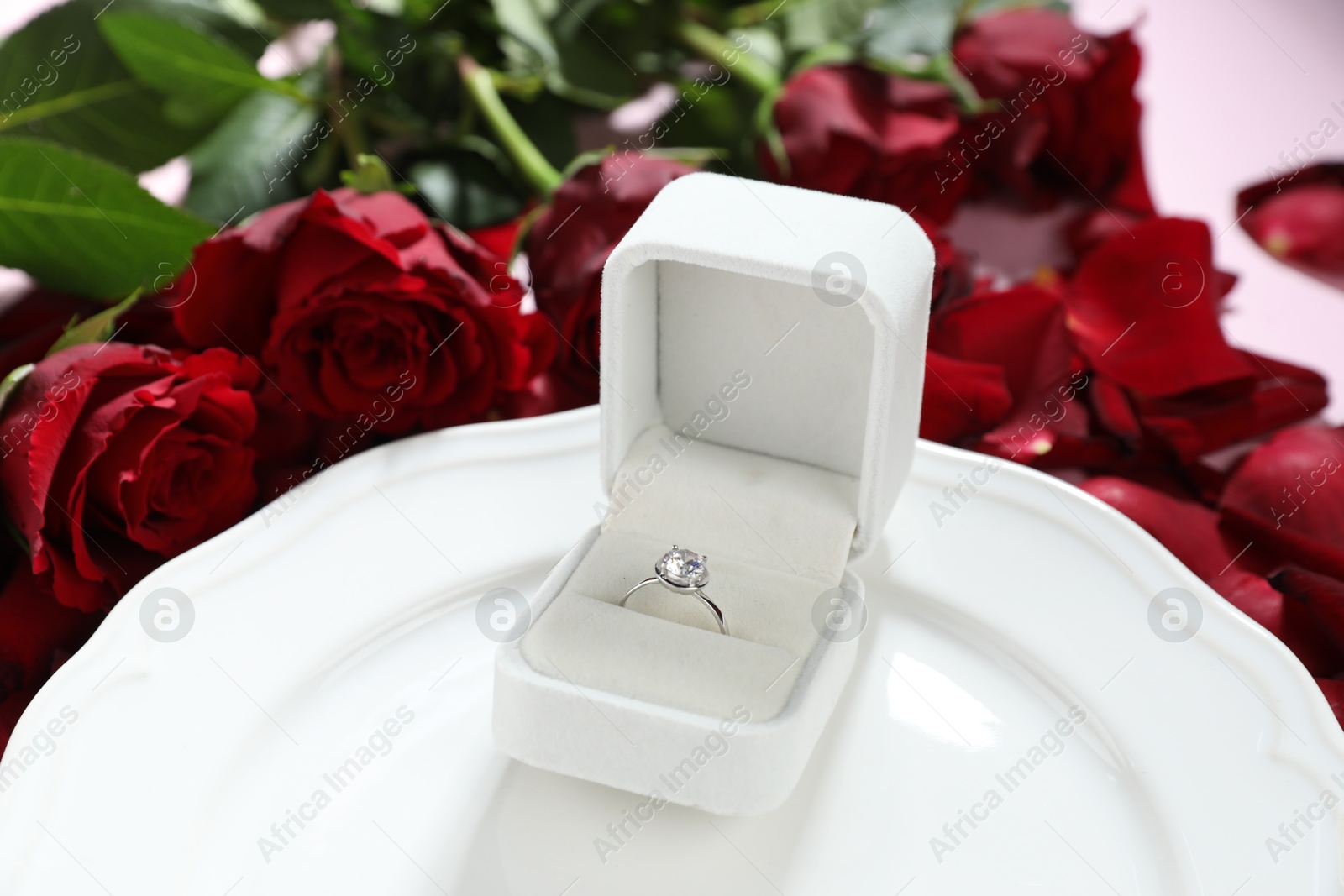 Photo of Beautiful setting for romantic dinner, engagement ring and rose petals on light table, closeup