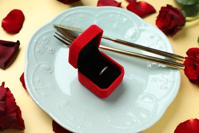 Photo of Beautiful setting for romantic dinner, engagement ring and roses on beige background, closeup