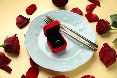 Photo of Beautiful setting for romantic dinner, engagement ring and roses on beige background, closeup