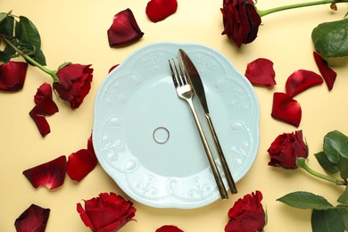 Photo of Beautiful setting for romantic dinner, engagement ring and roses on beige background, flat lay