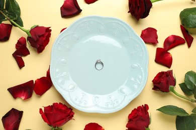 Beautiful setting for romantic dinner, engagement ring and roses on beige background, flat lay