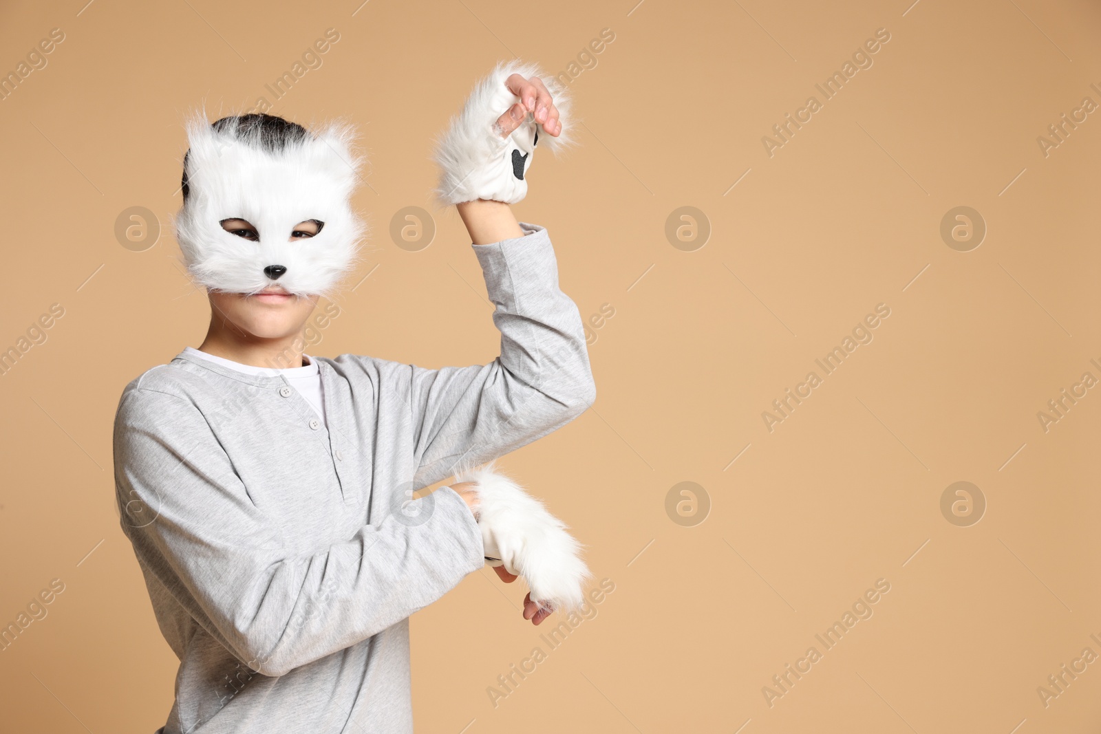 Photo of Quadrobics. Boy wearing cat mask and gloves on beige background, space for text