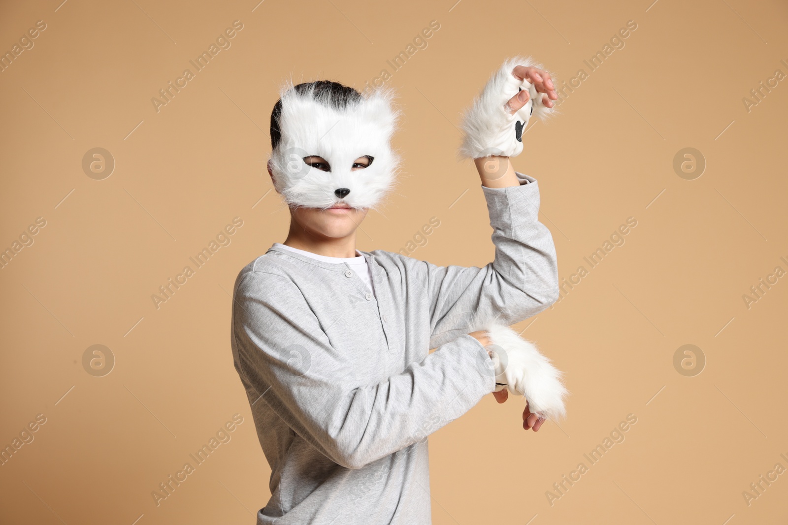 Photo of Quadrobics. Boy wearing cat mask and gloves on beige background