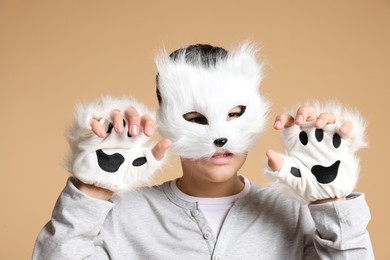 Photo of Quadrobics. Boy wearing cat mask and gloves on beige background