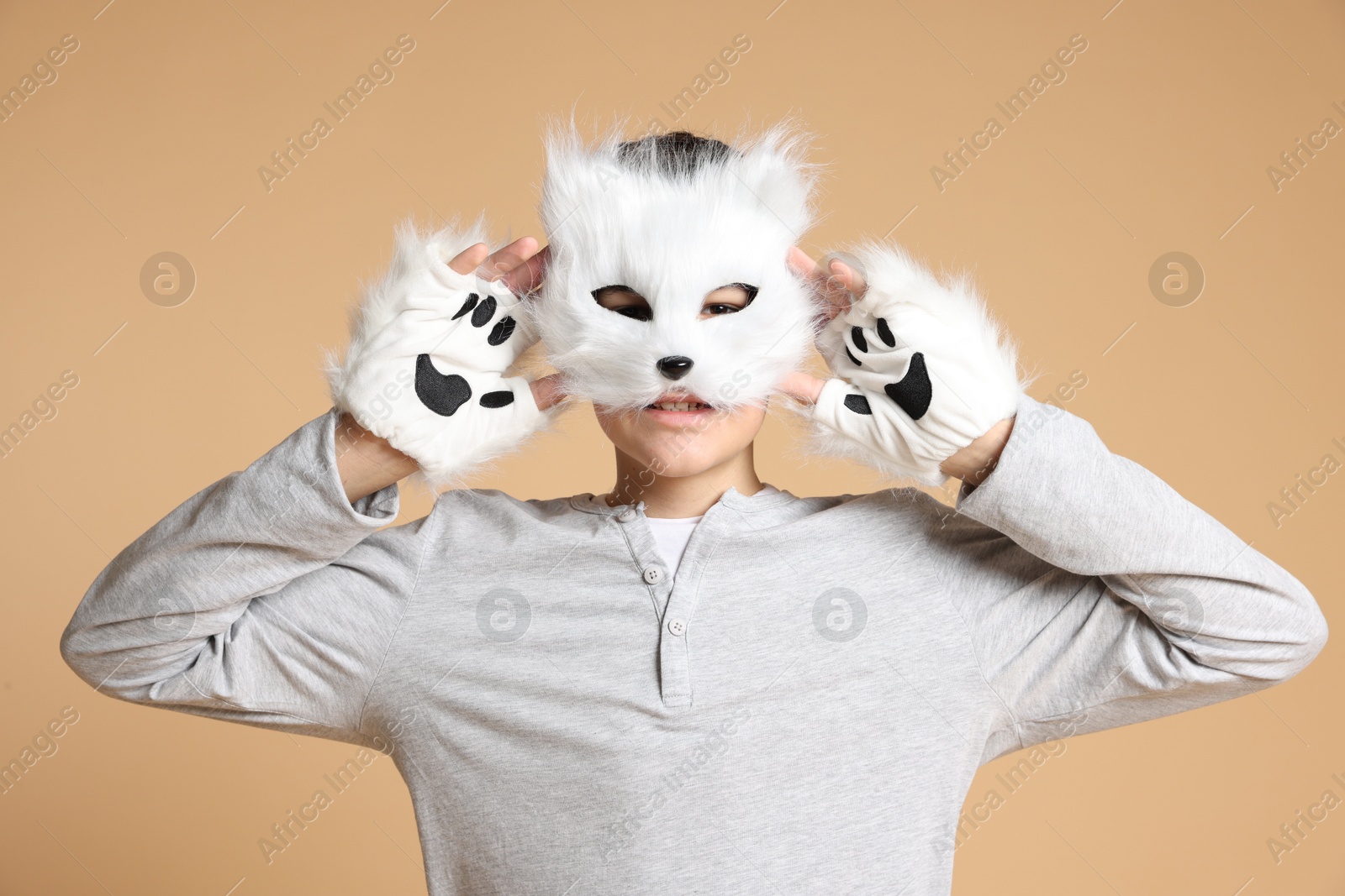 Photo of Quadrobics. Boy wearing cat mask and gloves on beige background