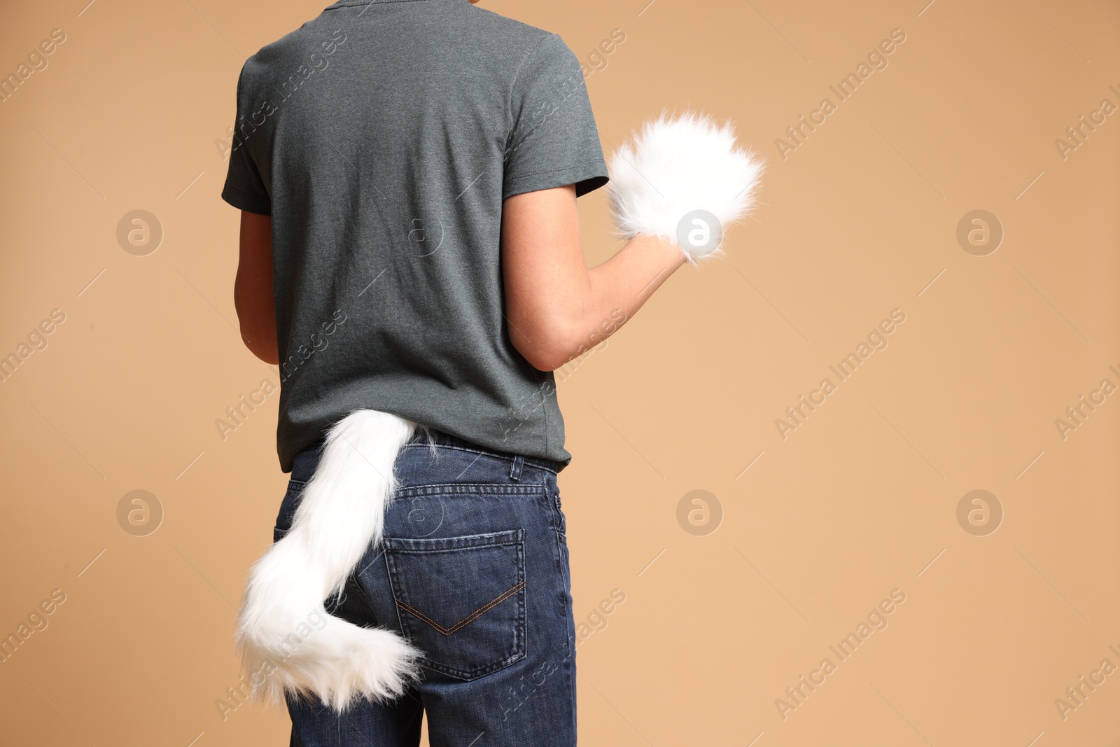 Photo of Quadrobics. Boy wearing cat gloves and tail on beige background, closeup. Space for text