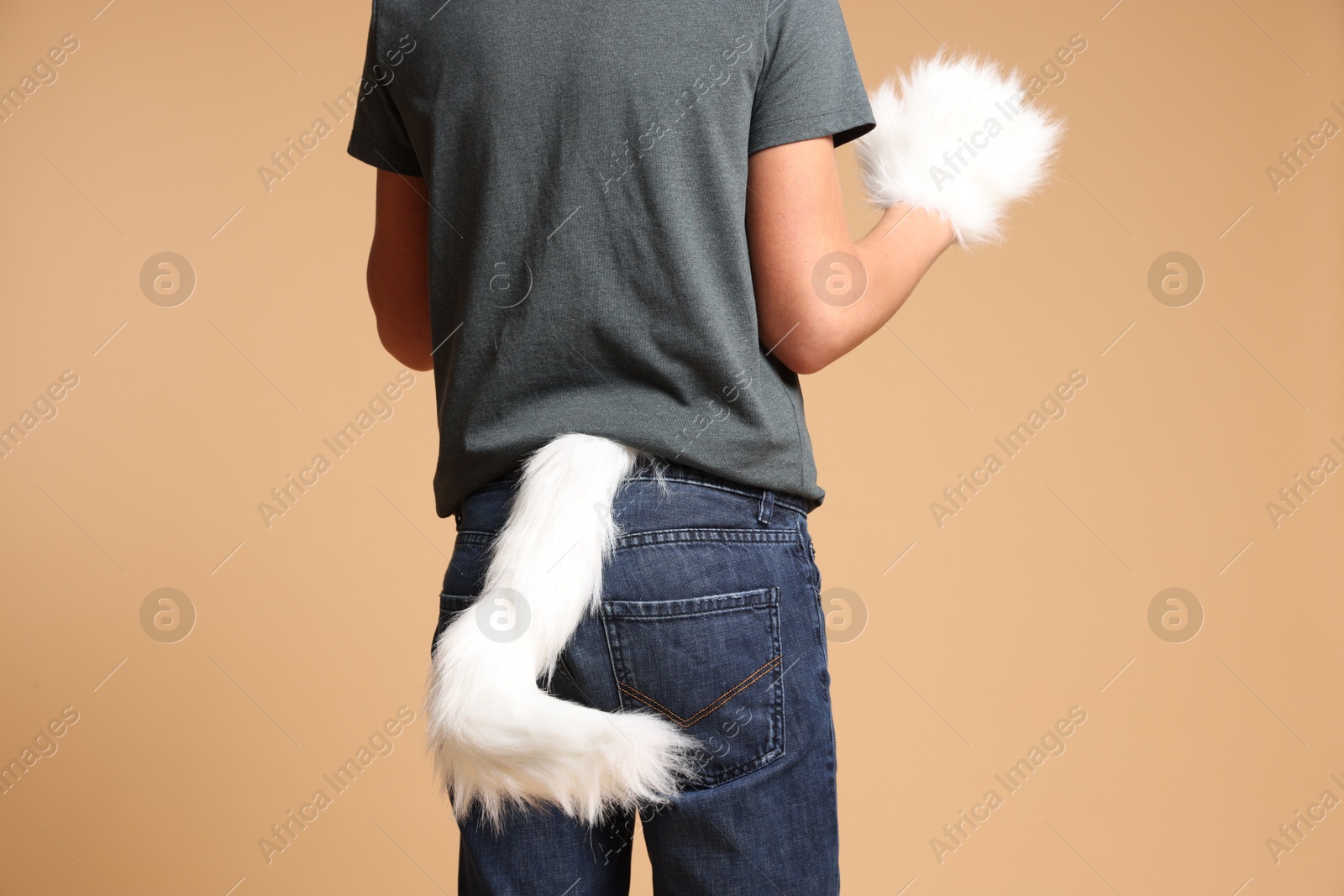 Photo of Quadrobics. Boy wearing cat gloves and tail on beige background, closeup