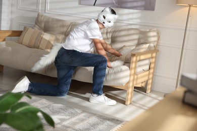 Quadrobics. Boy wearing cat mask, gloves and tail on sofa at home