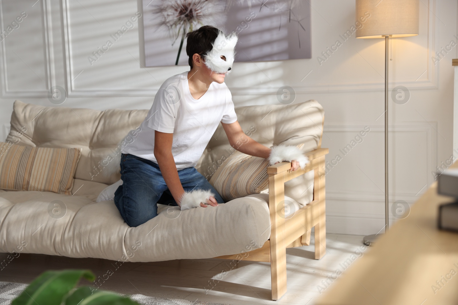 Photo of Quadrobics. Boy wearing cat mask, gloves and tail on sofa at home