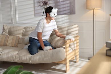 Photo of Quadrobics. Boy wearing cat mask, gloves and tail on sofa at home