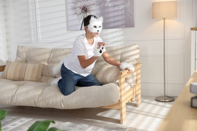 Quadrobics. Boy wearing cat mask, gloves and tail on sofa at home