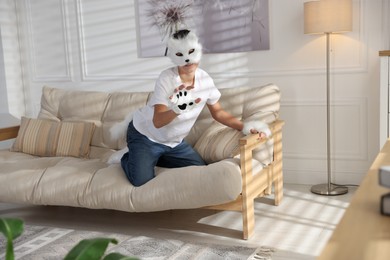 Photo of Quadrobics. Boy wearing cat mask, gloves and tail on sofa at home