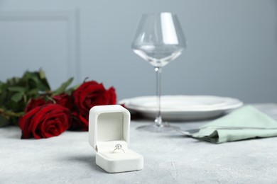 Photo of Beautiful setting for romantic dinner, engagement ring and roses on light table