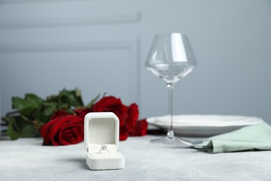 Photo of Beautiful setting for romantic dinner, engagement ring and roses on light table