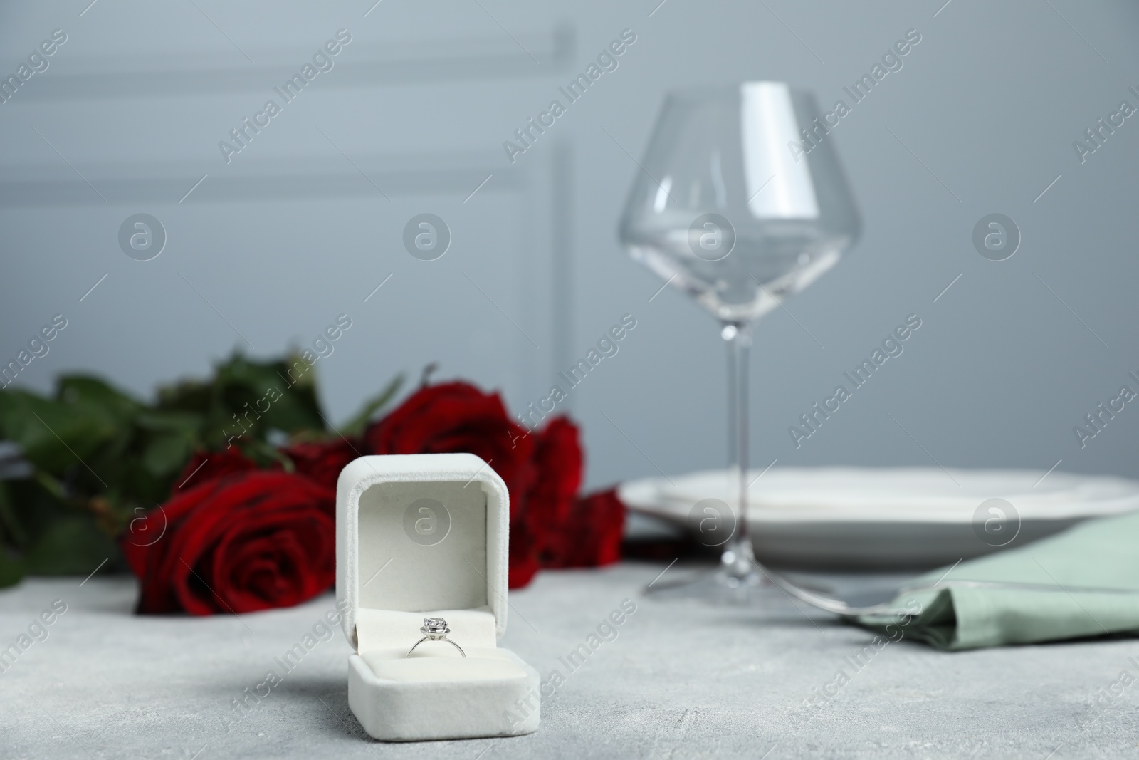 Photo of Beautiful setting for romantic dinner, engagement ring and roses on light table