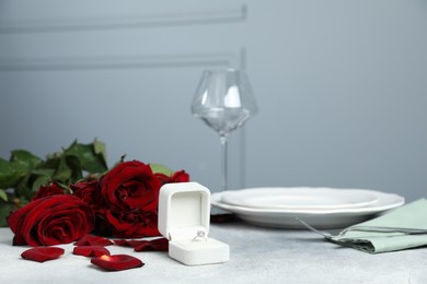 Photo of Beautiful setting for romantic dinner, engagement ring and roses on light table