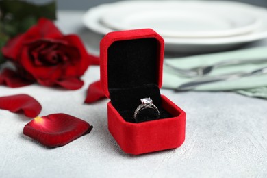 Photo of Beautiful setting for romantic dinner, engagement ring and rose on light table, closeup