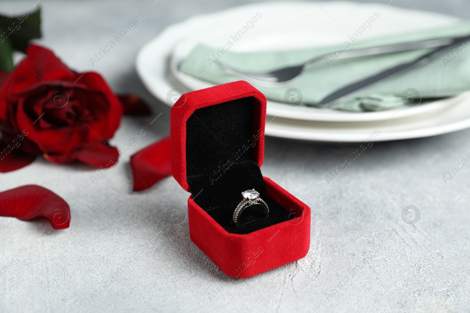 Photo of Beautiful setting for romantic dinner, engagement ring and rose on light table, closeup