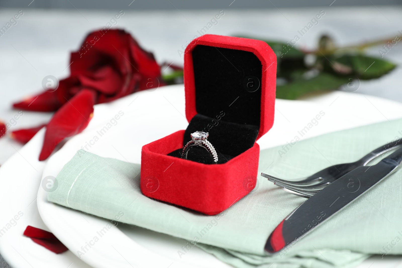 Photo of Beautiful setting for romantic dinner, engagement ring and rose on light table, closeup