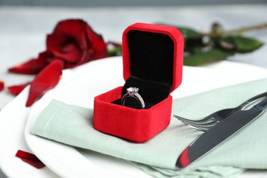 Photo of Beautiful setting for romantic dinner, engagement ring and rose on light table, closeup