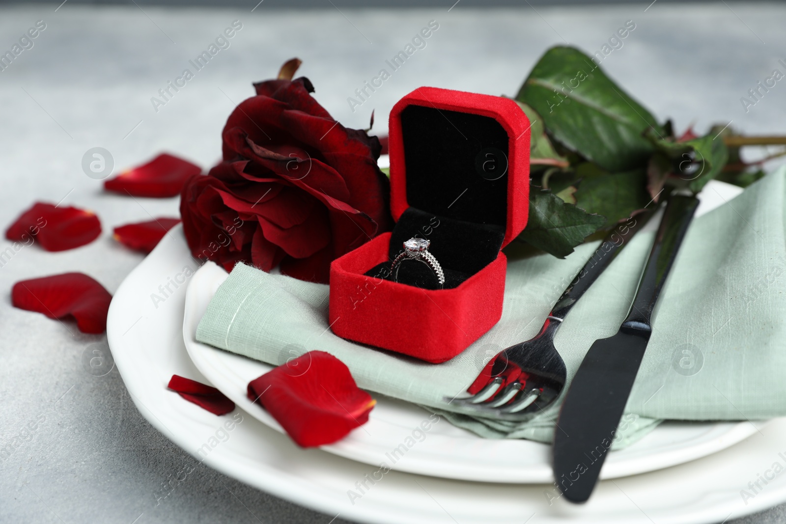 Photo of Beautiful setting for romantic dinner, engagement ring and rose on light table, closeup