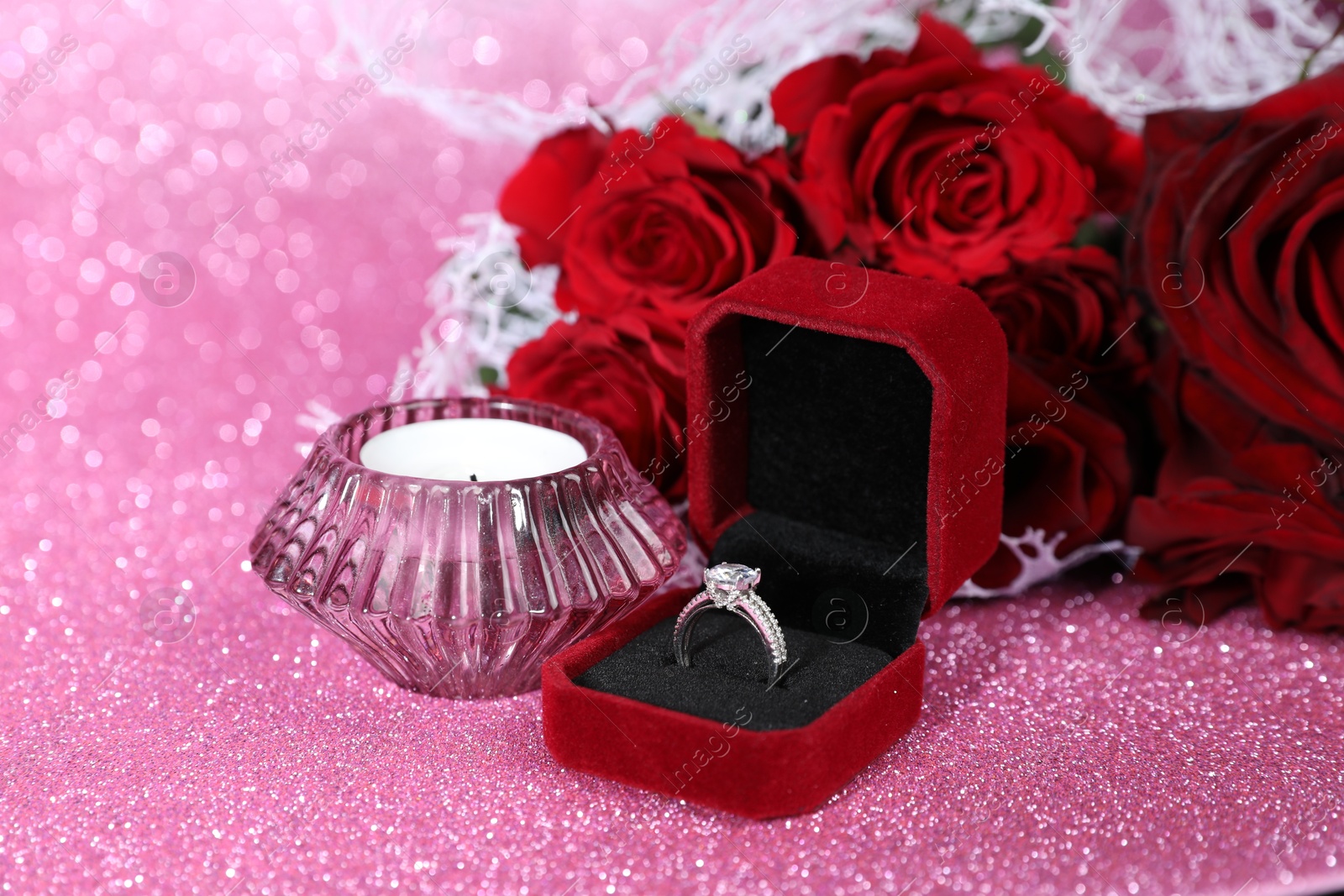 Photo of Engagement ring, candle and roses on pink background, closeup. Romantic gift