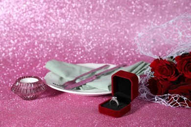 Photo of Beautiful setting for romantic dinner, engagement ring and roses on pink background