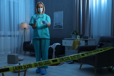 Photo of Forensic expert examining plastic bag with drug powder through magnifying glass at crime scene indoors