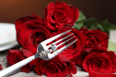 Photo of Fork with engagement ring against roses, closeup. Romantic dinner