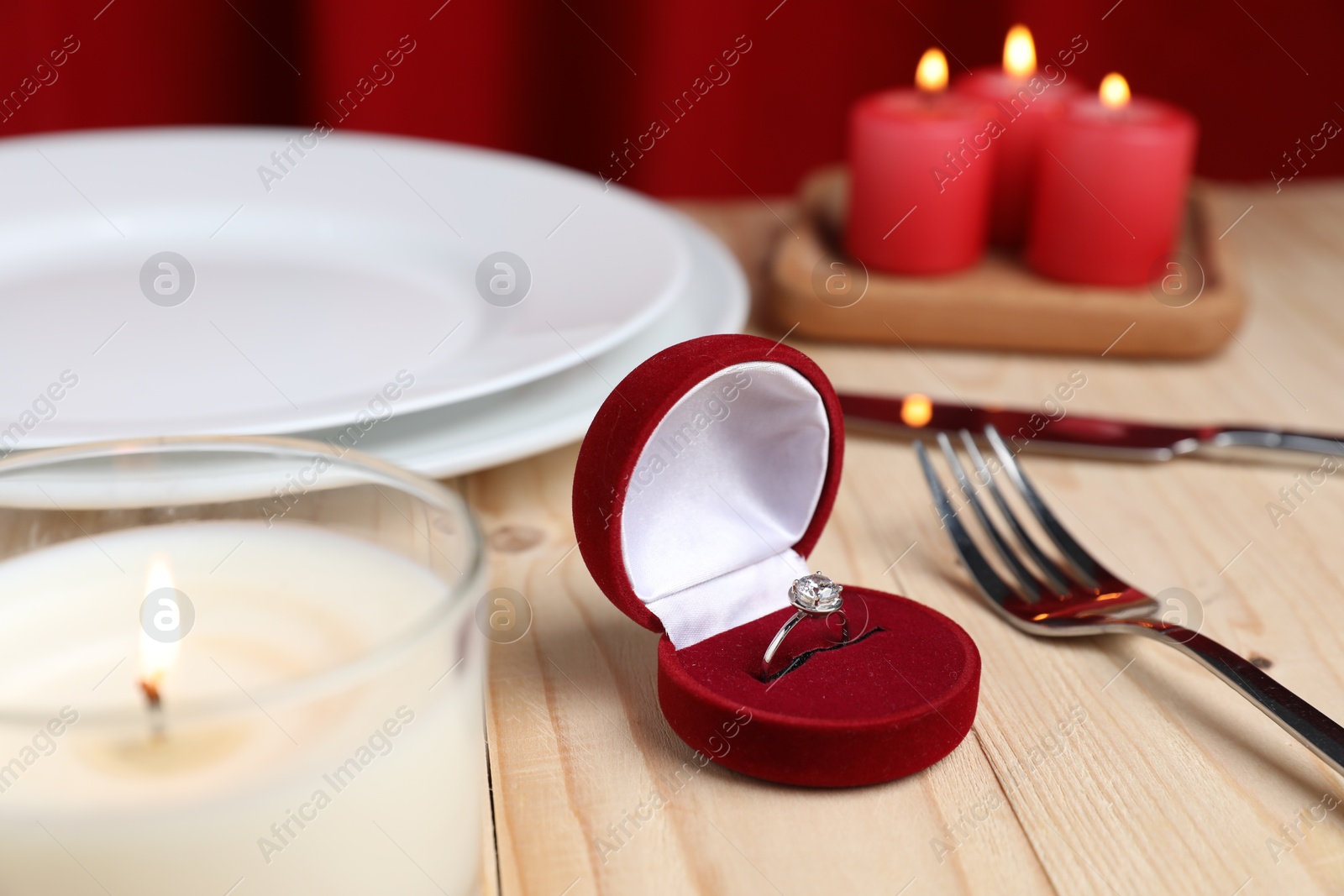 Photo of Beautiful setting for romantic dinner, engagement ring and burning candles on wooden table, closeup