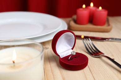 Photo of Beautiful setting for romantic dinner, engagement ring and burning candles on wooden table, closeup