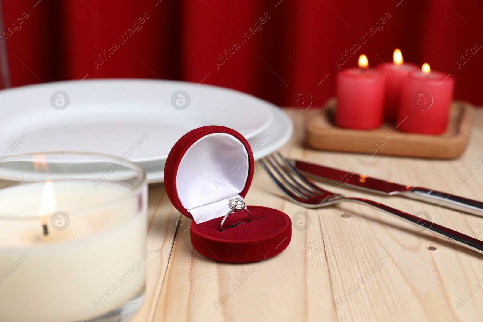 Photo of Beautiful setting for romantic dinner, engagement ring and burning candles on wooden table, closeup