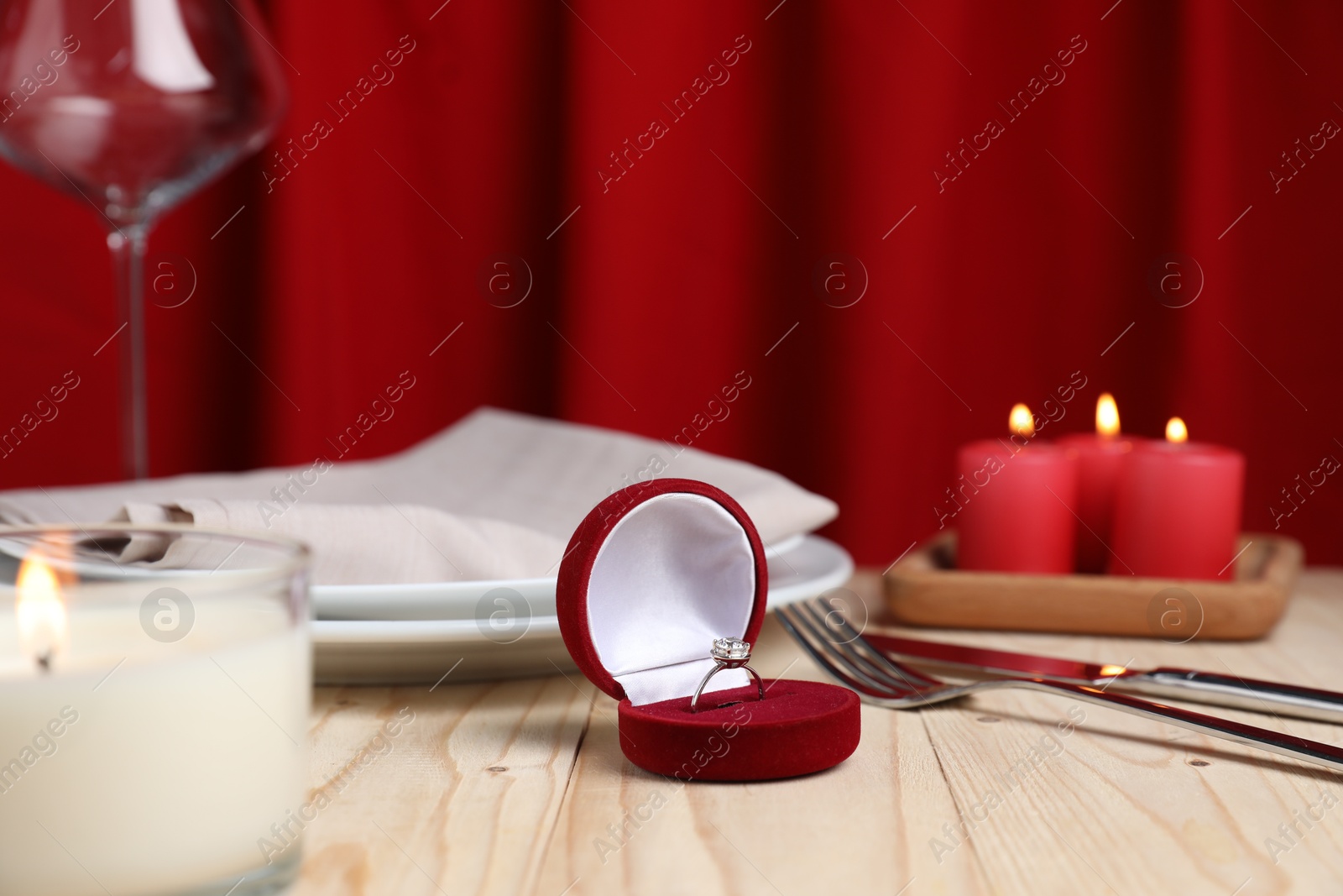 Photo of Beautiful setting for romantic dinner, burning candles and engagement ring on wooden table