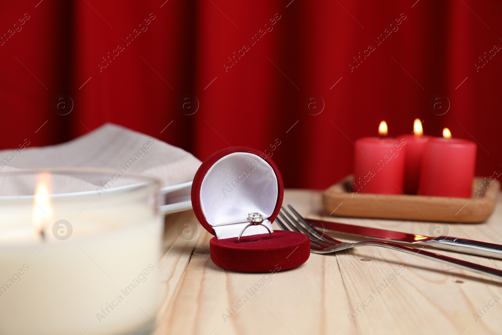 Photo of Beautiful setting for romantic dinner, engagement ring and burning candles on wooden table, closeup