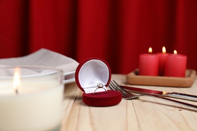 Photo of Beautiful setting for romantic dinner, engagement ring and burning candles on wooden table, closeup