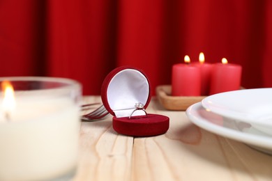 Photo of Beautiful setting for romantic dinner, engagement ring and burning candles on wooden table, closeup