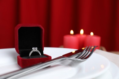 Photo of Beautiful setting for romantic dinner, engagement ring and burning candles on table, closeup