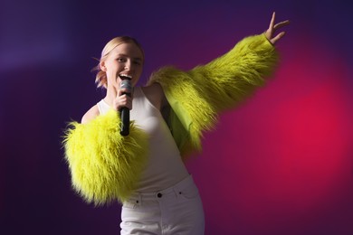 Photo of Talented singer in faux fur performing on purple background with pink light