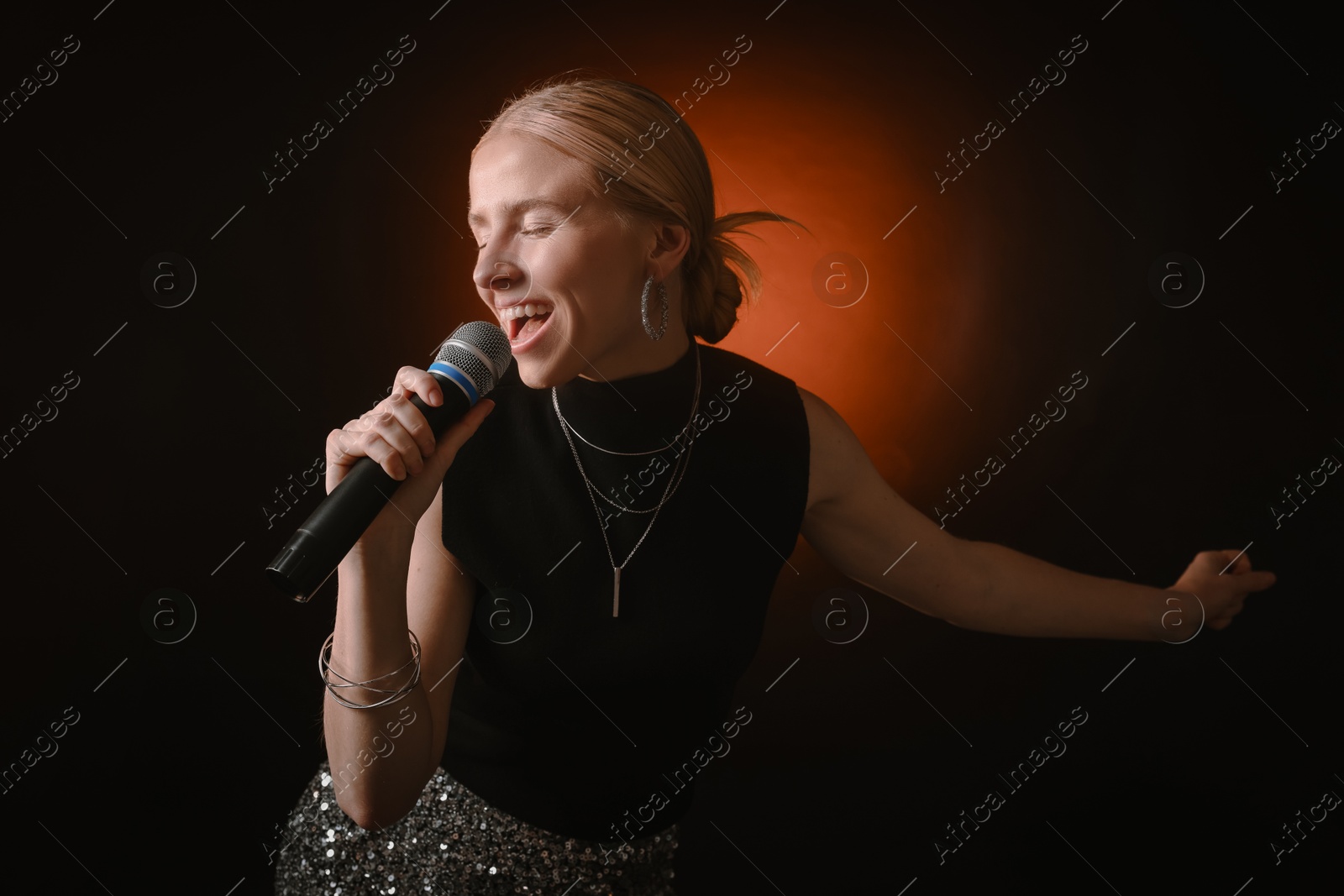 Photo of Beautiful singer performing on dark background with color light